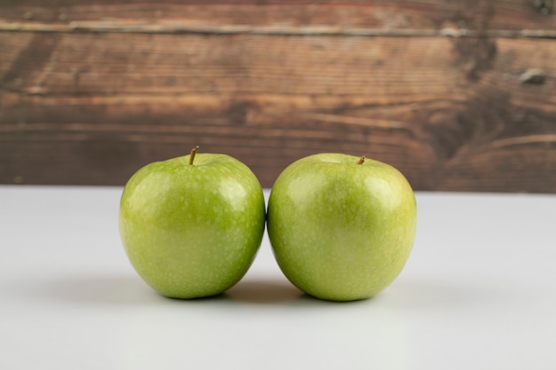 Dos manzanas verdes maduras colocadas sobre la mesa blanca.