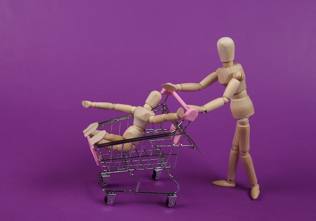 Dos marionetas de madera con carrito de supermercado comprando juntos sobre fondo morado