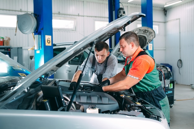 Dos mecánicos guapos en uniforme están trabajando en auto servicio