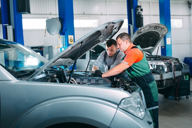 Dos mecánicos guapos en uniforme están trabajando en auto servicio