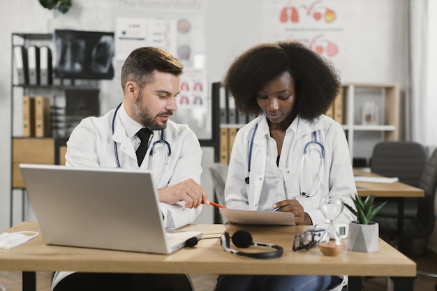 Dos médicos diversos reunidos con laptop y papeles.