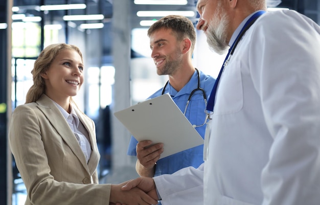 Dos médicos y una paciente se dan la mano antes de la consulta en la oficina de un centro médico moderno.