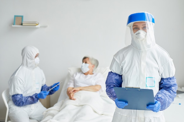 Dos médicos profesionales con trajes protectores con guantes, máscaras y gafas que trabajan con pacientes ancianos en la sala de enfermedades infecciosas