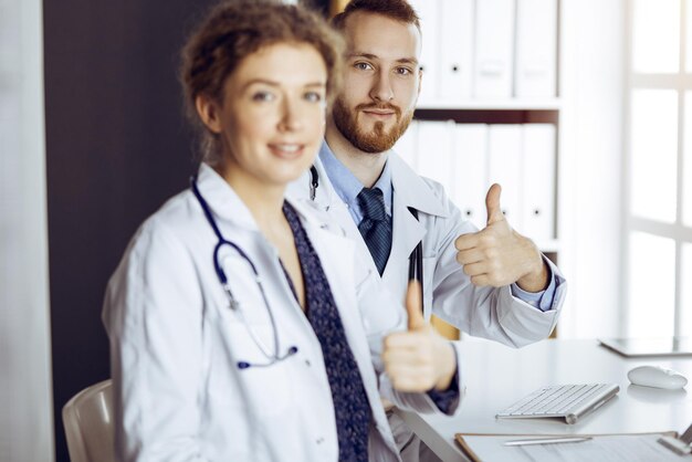 Dos médicos sentados con los pulgares hacia arriba en el consultorio del hospital. Ayuda médica, contrarrestando la infección viral y el concepto de medicina.