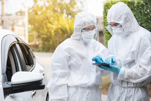 Dos médicos con traje protector PPE están usando una tableta para verificar la información del brote de covid-19. Concepto de coronavirus y asistencia sanitaria.