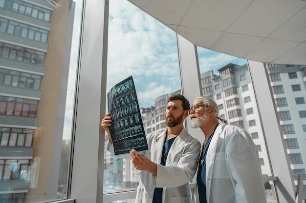 Foto dos médicos en uniforme miran y discuten una radiografía o una resonancia magnética de la columna del paciente en la clínica de medicina