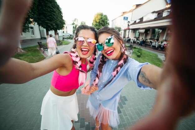 Dos mejores amigas de moda y hermosas con anteojos, posando haciendo el yo general, mostrando a todos su estilo de vida, pasan el tiempo alegremente. Mujeres con gafas de sol Descansa en la ciudad. Fin de semana.