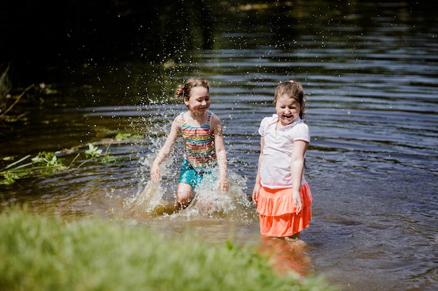 Dos mejores amigas niñas chapoteando en el agua del lago el día de verano