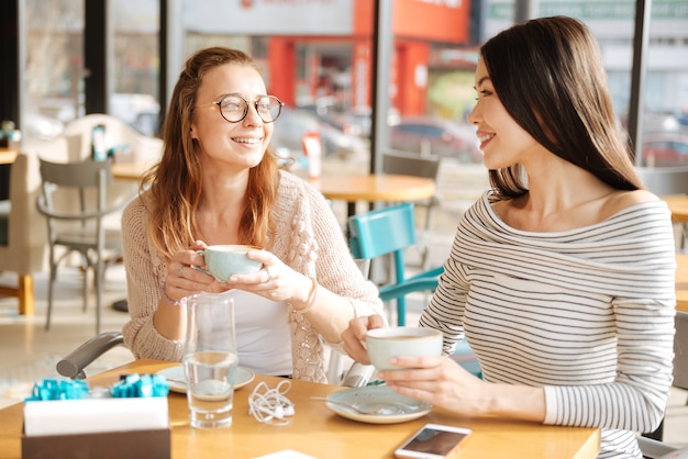 Dos mejores amigas. Pareja de novias se miran mientras están sentados en el café y sosteniendo tazas con café.