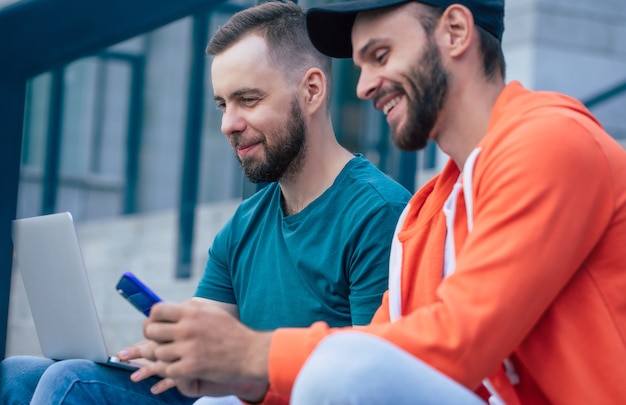Dos mejores amigos al aire libre con smartphone y portátil están trabajando en las escaleras