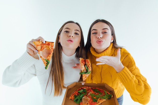 Dos mejores amigos comiendo pizza apetitosa. Chicas sonriendo, mirando a la cámara y posando.