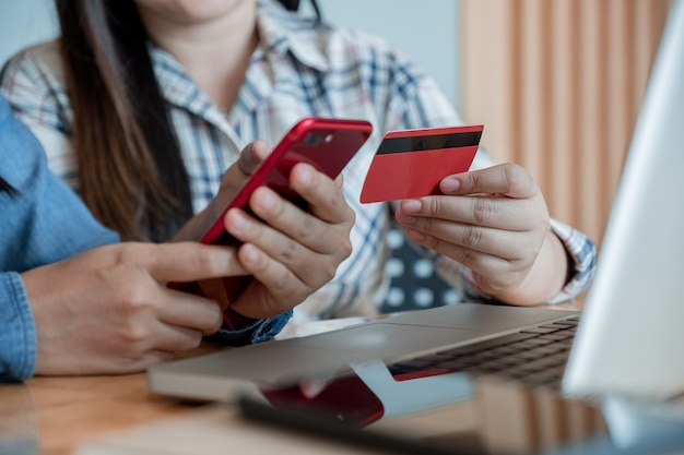 Foto dos mejores manos felices de las novias que sostienen el teléfono elegante y que usan la tarjeta de crédito para las compras en línea