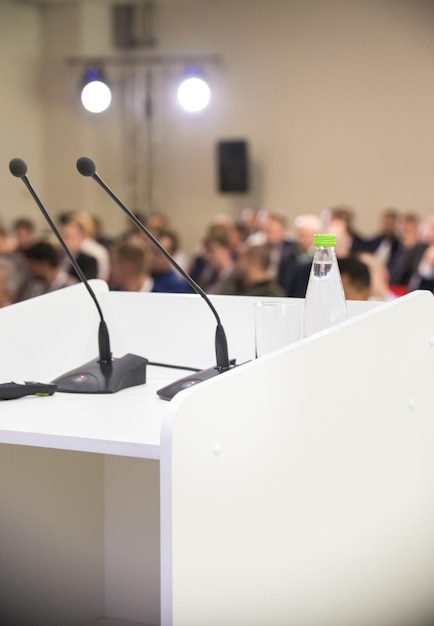 Dos micrófonos en la mesa y una botella de agua. Conferencia de negocios. Salón lleno de gente