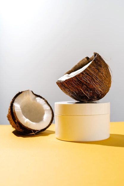Dos mitades de coco y un frasco de cosméticos sobre un fondo amarillo y gris