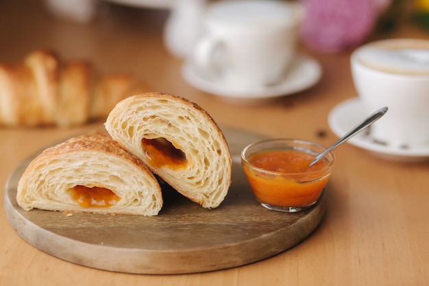 Dos mitades de croissant recién desnudo sobre tabla de madera con deliciosa mermelada de albaricoque casera.