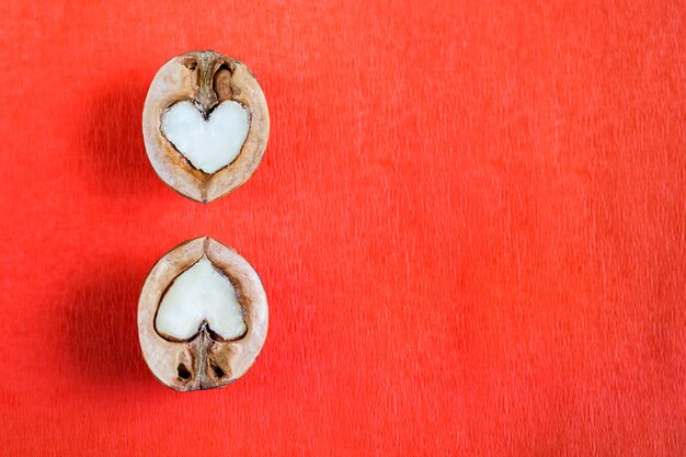 Dos mitades de nuez en forma de corazón se encuentran una sobre la otra sobre fondo de papel con textura roja.