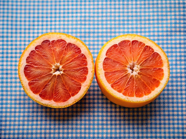 Foto dos mitades de pomelo rojo recién cortado colocadas en tela a cuadros azul y blanca