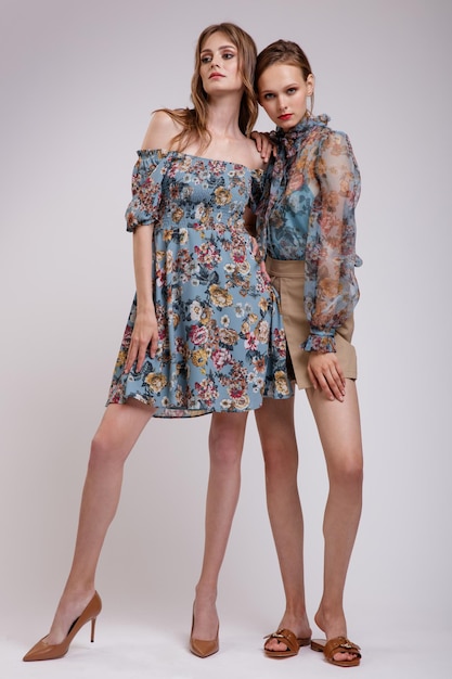 Dos modelos de alta moda en blusa azul transparente con estampado de flores vestido beige shorts