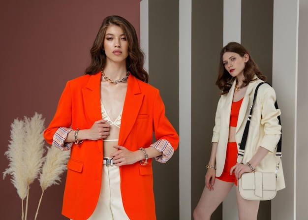 Dos modelos de moda en naranja y blanco crema se ve chaqueta blazer shorts top bolso