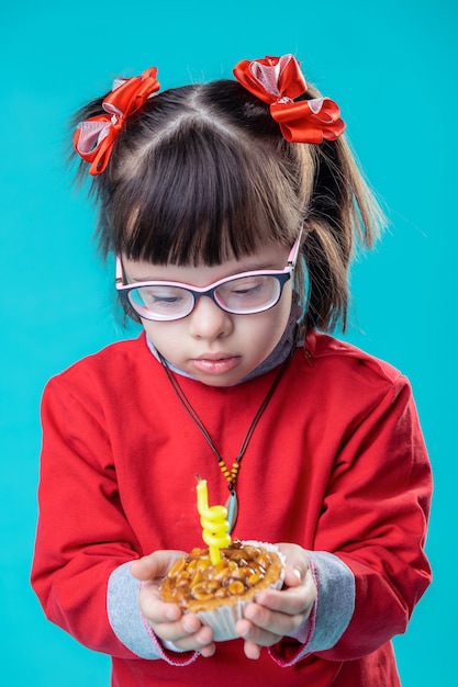 Dos moños rojos. Niña en todo traje rojo de pie contra la pared azul con muffin en sus manos