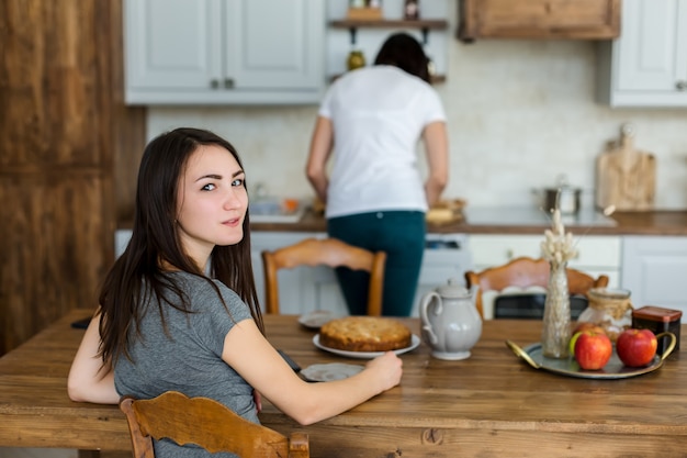 Foto dos morenas de chicas están bebiendo té con pastel y dulces en la mesa.