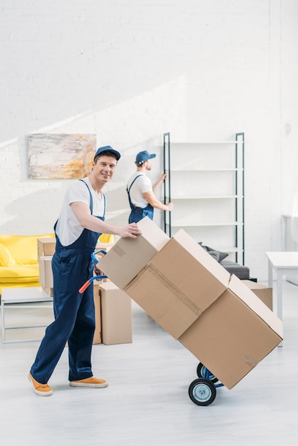 Foto dos motores en uniforme que transportan cajas de cartón y muebles en el apartamento