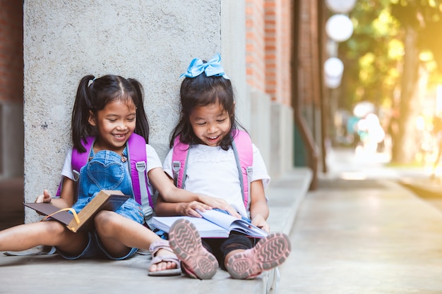 Dos muchachas asiáticas lindas del alumno que leen un libro juntos en la escuela con la diversión y la felicidad