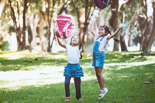 Dos muchachas asiáticas lindas del niño que se divierten para jugar y que lanzan su mochila al aire junto