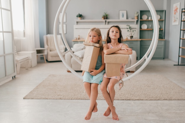 Dos muchachas felices en hermosos vestidos en columpio con cajas de regalo en sus manos