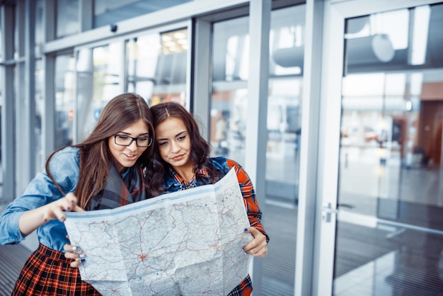 Dos muchachas hermosas jóvenes están estudiando y mirando el mapa.