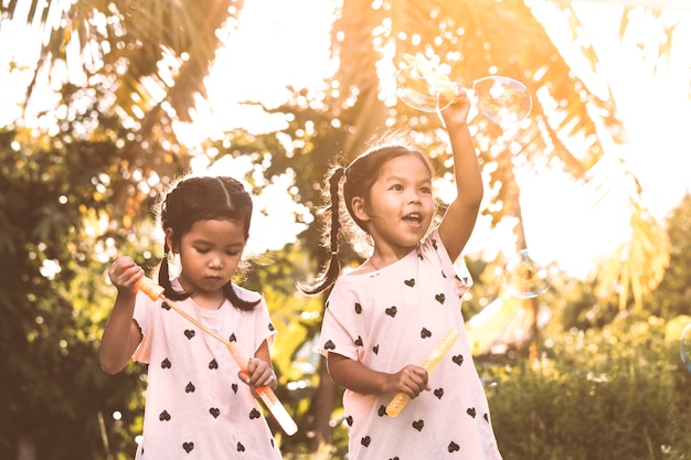 Dos muchachas lindas del niño asiático que se divierten para jugar con las burbujas juntas en al aire libre al atardecer