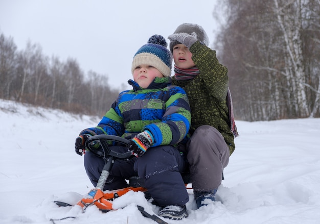 Dos muchachos de apariencia europea trineos en la nieve en el bosque mientras camina