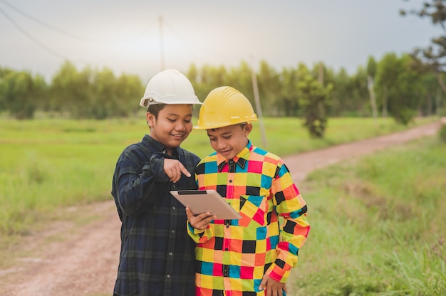 Dos muchachos asiáticos con casco con tableta de pie fuera de la puerta, ingeniero de concepto o control de construcción de capataz, escuela de estudio de collage de educación