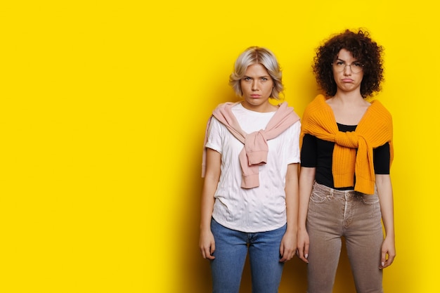 Dos mujer de pelo rizado posando molesto y triste en una pared amarilla