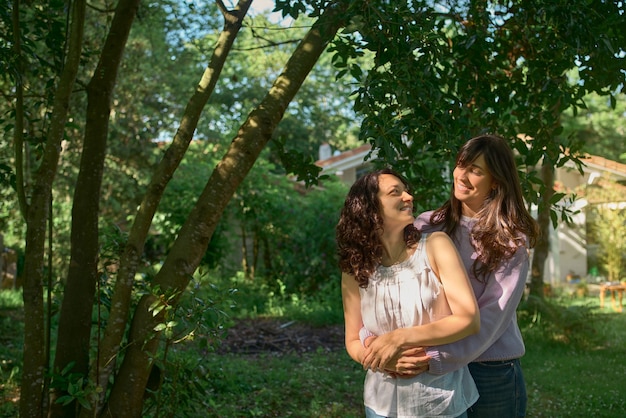 Dos mujeres se abrazan enamorados mirando el uno al otro sonriendo con árboles en el fondo