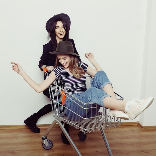 Dos mujeres adolescentes hermosas felices conduciendo el carrito de compras en el interior