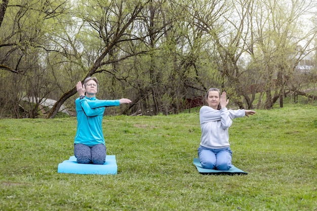 Dos mujeres adultas de 50 años haciendo yoga en un parque al aire libre