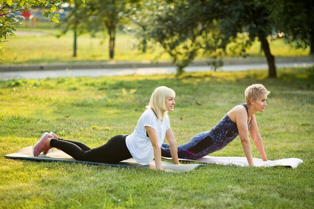 dos mujeres adultas de edad yoga al aire libre en verano en el parque