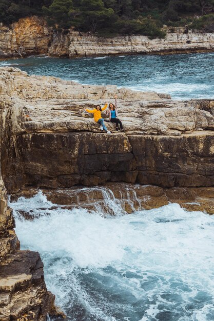 Dos mujeres adultas jóvenes en el acantilado mirando el mar de tormenta