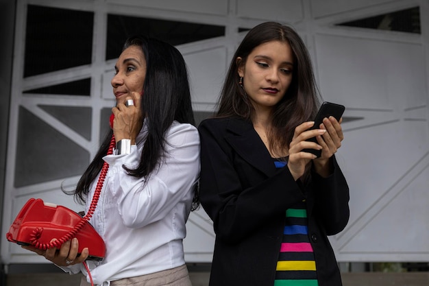 Dos mujeres adultas latinoamericanas, madre e hija, utilizan dos tecnologías de diferentes épocas.
