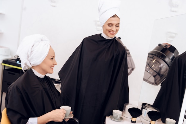 Dos mujeres adultas con toallas en sus cabezas tomando café.