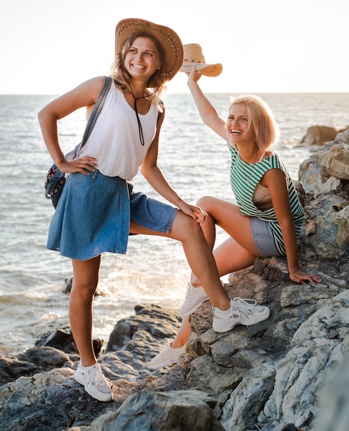 Dos mujeres alegres jóvenes en sombreros de hipsters en una roca en la costa del mar.