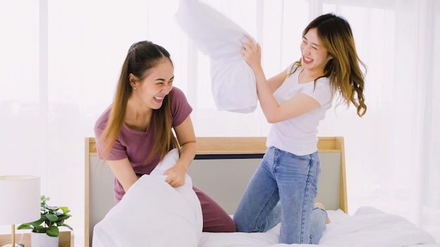 Dos mujeres asiáticas felices y atractivas que tienen una pelea de almohadas con sonrisas se ríen y se divierten juntas en la cama LGBTQ o parejas lesbianas juegan peleas de almohadas juntas en el dormitorio Concepto de pareja del mismo sexo