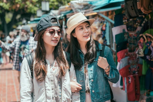 dos mujeres asiáticas felices caminando en el mercado verde al aire libre de méxico en los ángeles. alegres curiosos jóvenes amigas viajeros calle olvera mirando de compras bajo el sol. turismo de hermanas sonrientes
