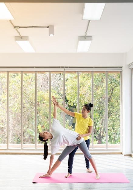 Dos mujeres asiáticas felices en posturas de yoga en estudio de yoga con escenario de luz natural / concepto de ejercicio / práctica de yoga / espacio de copia / estudio de yoga