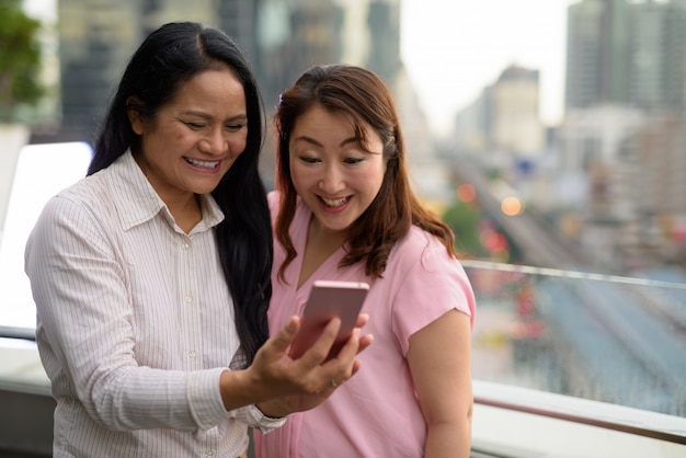 Dos mujeres asiáticas maduras juntas contra la vista de la ciudad