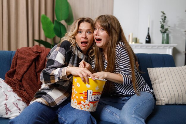 Dos mujeres asustadas en el sofá viendo una película de terror en la televisión en casa