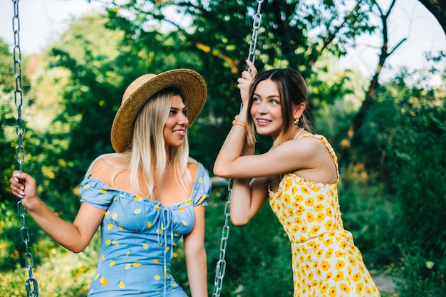 Dos mujeres atractivas de pie cerca de columpio en el jardín en un día soleado de verano.