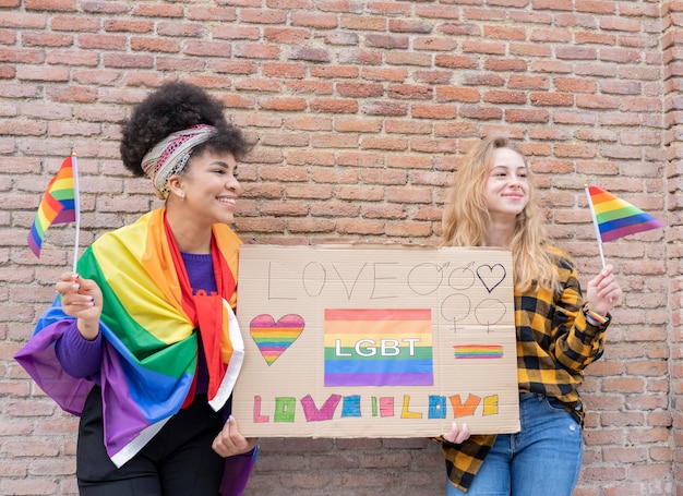 Dos mujeres con bandera del orgullo gay en la calle, con megáfono y pancarta demostrando