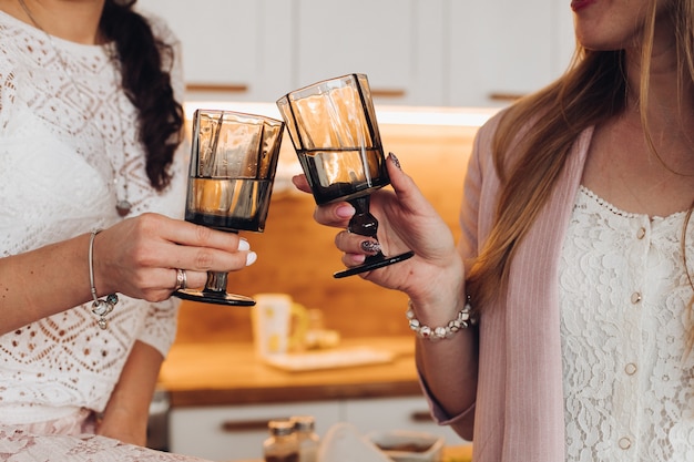 Dos mujeres beben agua con vasos en la cocina juntas